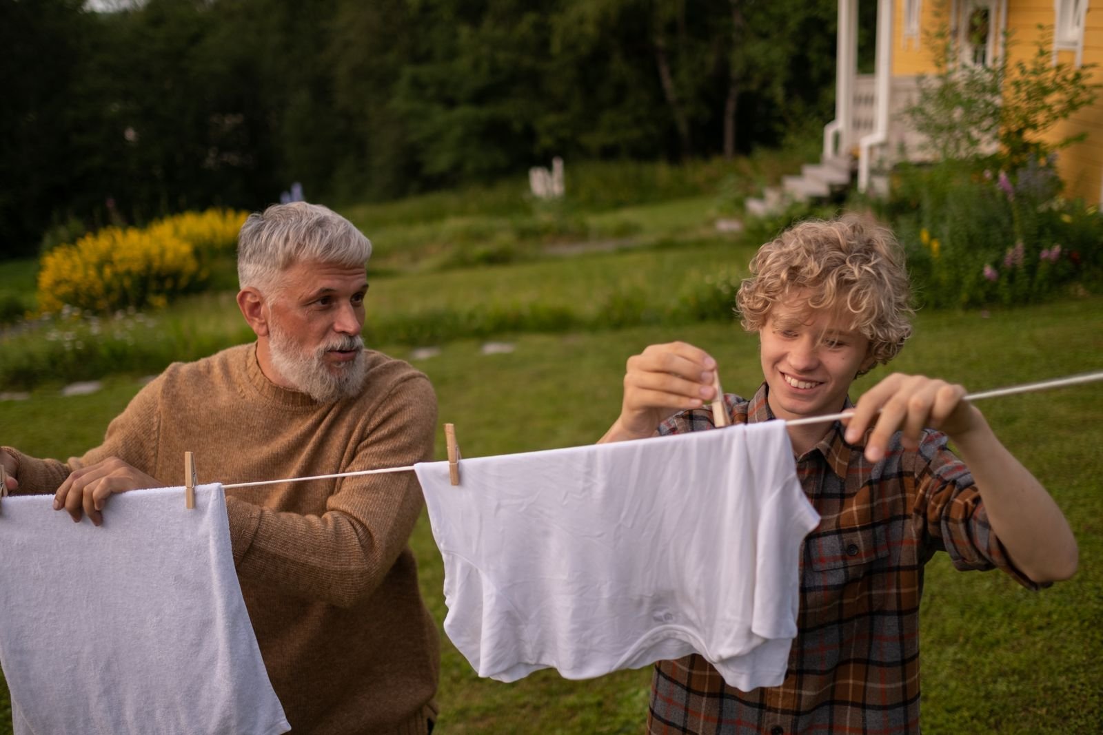 An adult and a teenage boy hanging laundry on a clothesline outdoors
