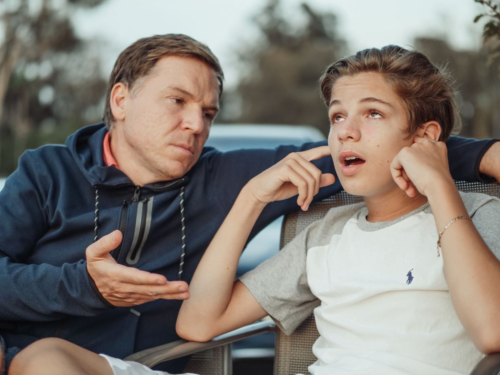 An adult talking with a teenage boy while they sit together on a sofa