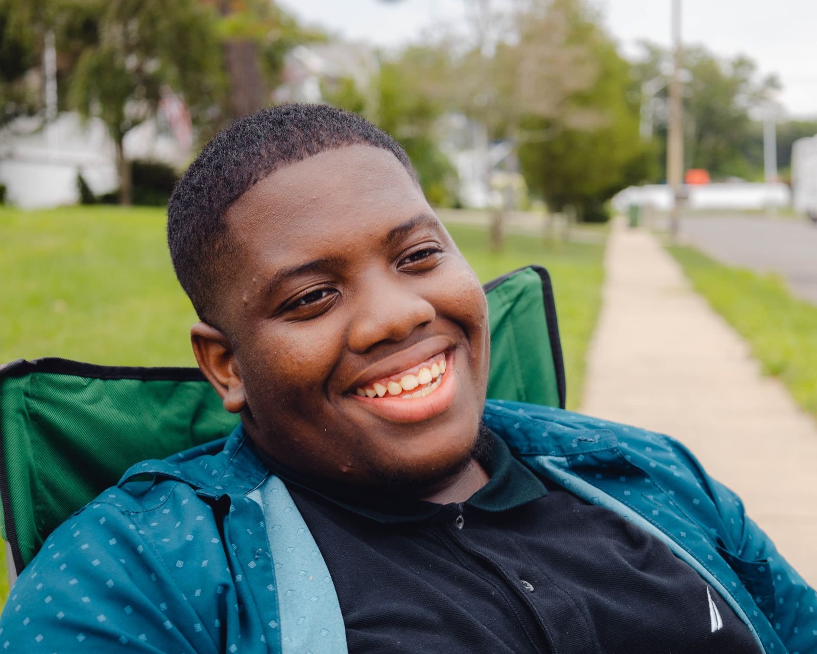 A smiling teenage boy sitting outdoors on a sunny day