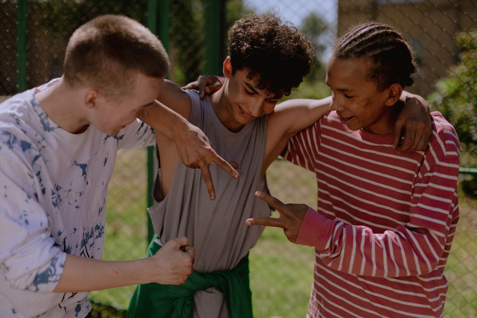 Three teenage boys laughing together outdoors with their arms around each other