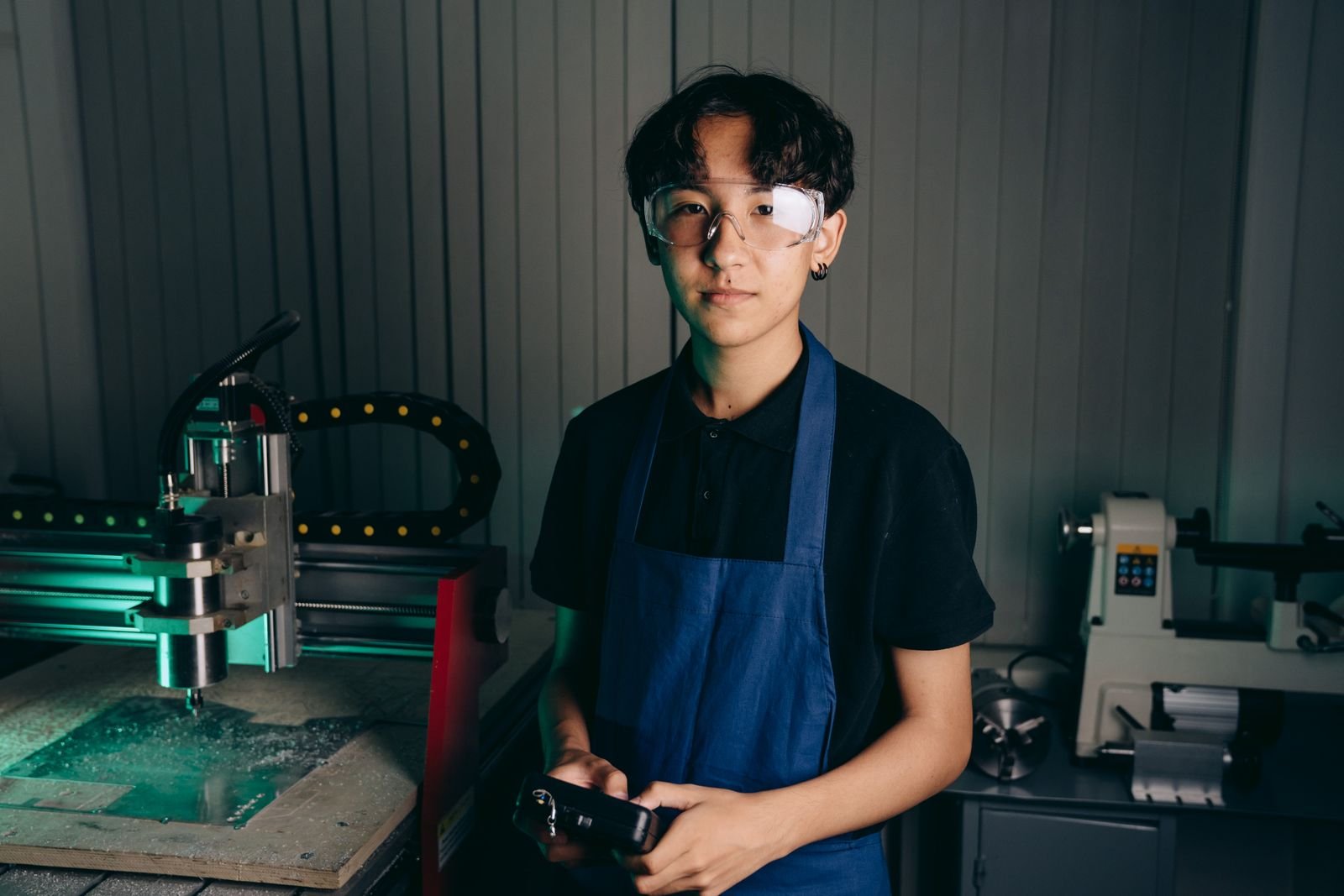 A young man wearing an apron and safety glasses standing in a workshop